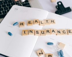 Scrabble tiles spelling 'Health Insurance' on planner with pills and laptop, symbolizing healthcare planning.